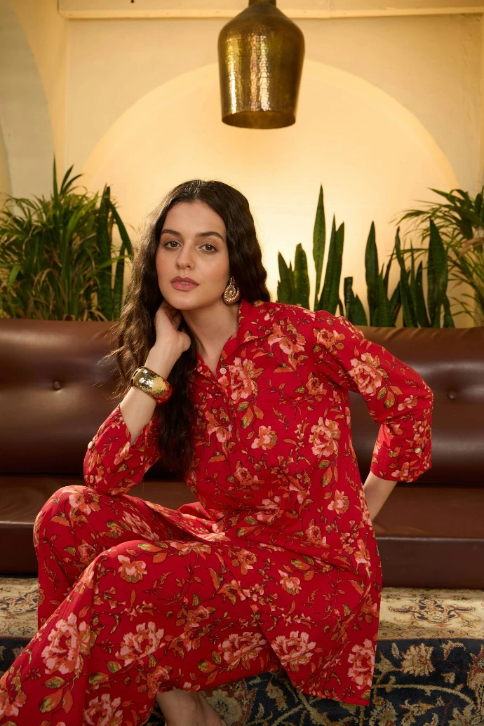 Woman in red floral outfit sitting on brown sofa.